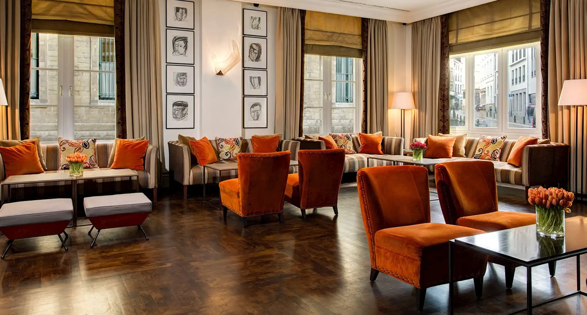 The lobby of Amigo Hotels in Brussels features orange chairs and tables, creating a warm and inviting atmosphere.