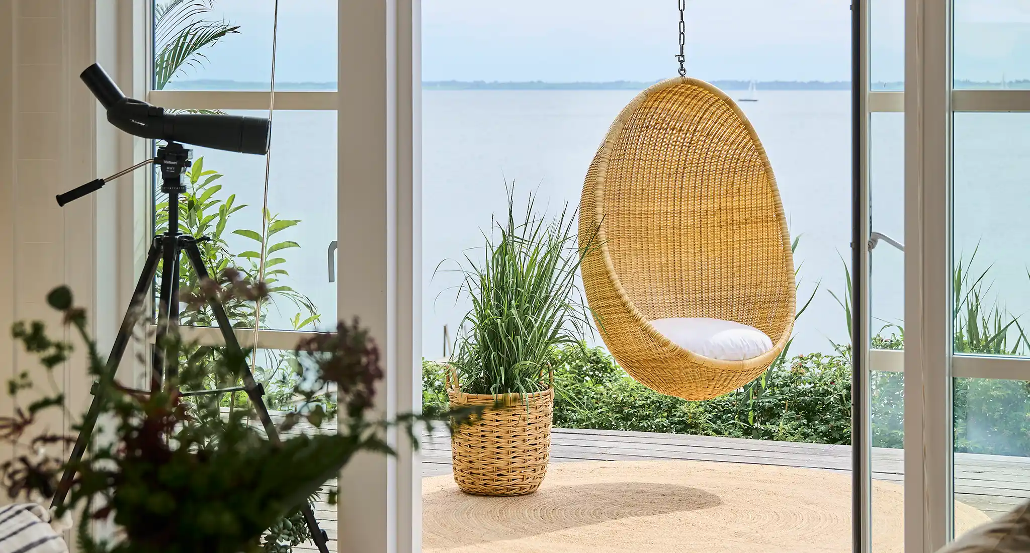 A hanging chair suspended in front of a window with a view of the water, part of an outdoor furniture supply project for a residential property in Hong Kong.